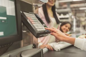 Cheerful mother and daughter are locating nearby tape in supermarket on background. Close up of female hand, using special keyboard