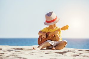 Little boy sitting on the beach playing guitar
