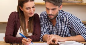 Happy young couple reading and analyzing bills sitting at table. Young couple in casual discussing home economics. Young couple calculating their expenses and incomes.