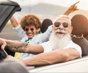 Happy senior multiracial couple having fun on road trip summer vacation inside convertible car