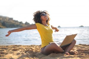 Young woman sitting at the beach, using her laptop