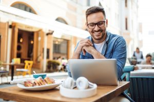 Handsome smiling modern young man using laptop at cafe